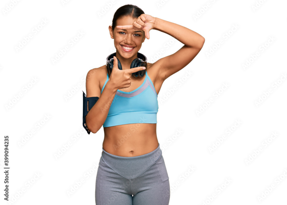 Beautiful hispanic woman wearing sportswear and headphones smiling making frame with hands and fingers with happy face. creativity and photography concept. Beautiful hispanic woman wearing sportswear and headphones smiling making frame with hands and fingers with happy face. creativity and photography concept.