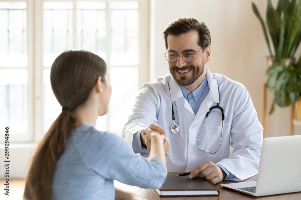 Smiling male GP shake hand of female patient at consultation in clinic get acquainted at meeting. Happy man doctor or physician handshake woman client close health insurance deal. Healthcare concept. Smiling male GP shake hand of female patient at consultation in clinic get acquainted at meeting. Happy man doctor or physician handshake woman client close health insurance deal. Healthcare concept.
