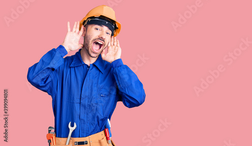 Young hispanic man wearing worker uniform smiling cheerful playing peek a boo with hands showing face. surprised and exited © Krakenimages.com