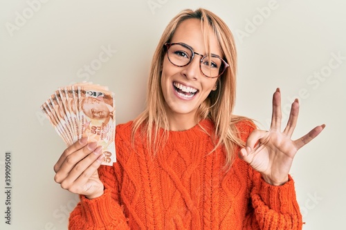 Canvas-taulu Beautiful blonde woman holding 50 turkish lira banknotes doing ok sign with fing
