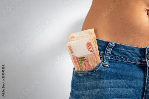 From the front pocket of the girl's jeans stick out buy 5 thousand Russian rubles. Copy space, horizontal photo