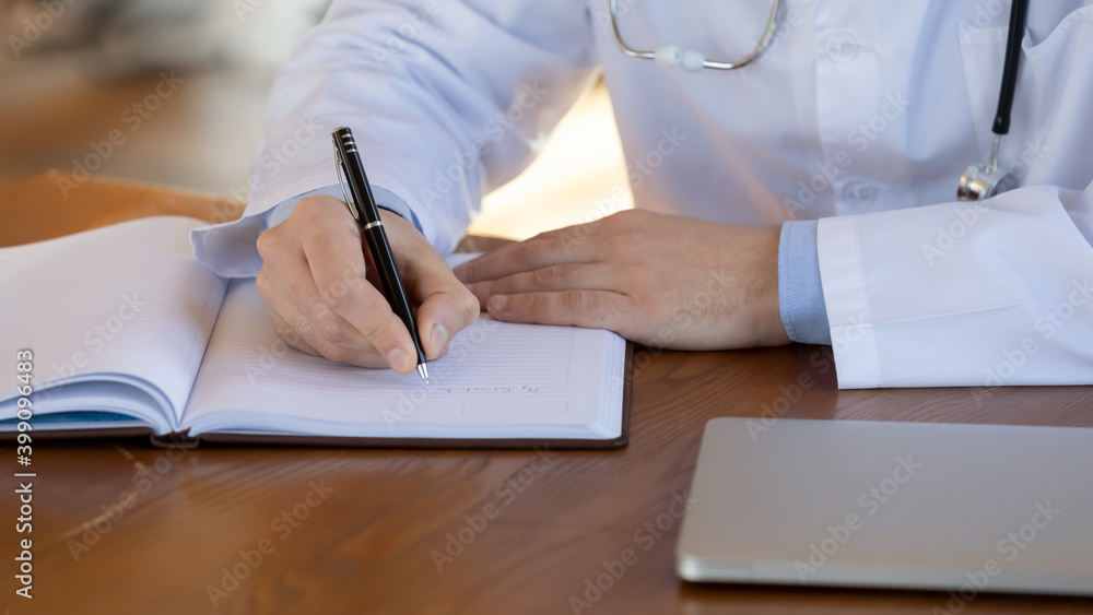 Wide banner view of male doctor in white medical uniform sit at desk in clinic make note in journal. Man GP or physician write fill patient or client illness anamnesis in notebook. Wide banner view of male doctor in white medical uniform sit at desk in clinic make note in journal. Man GP or physician write fill patient or client illness anamnesis in notebook.