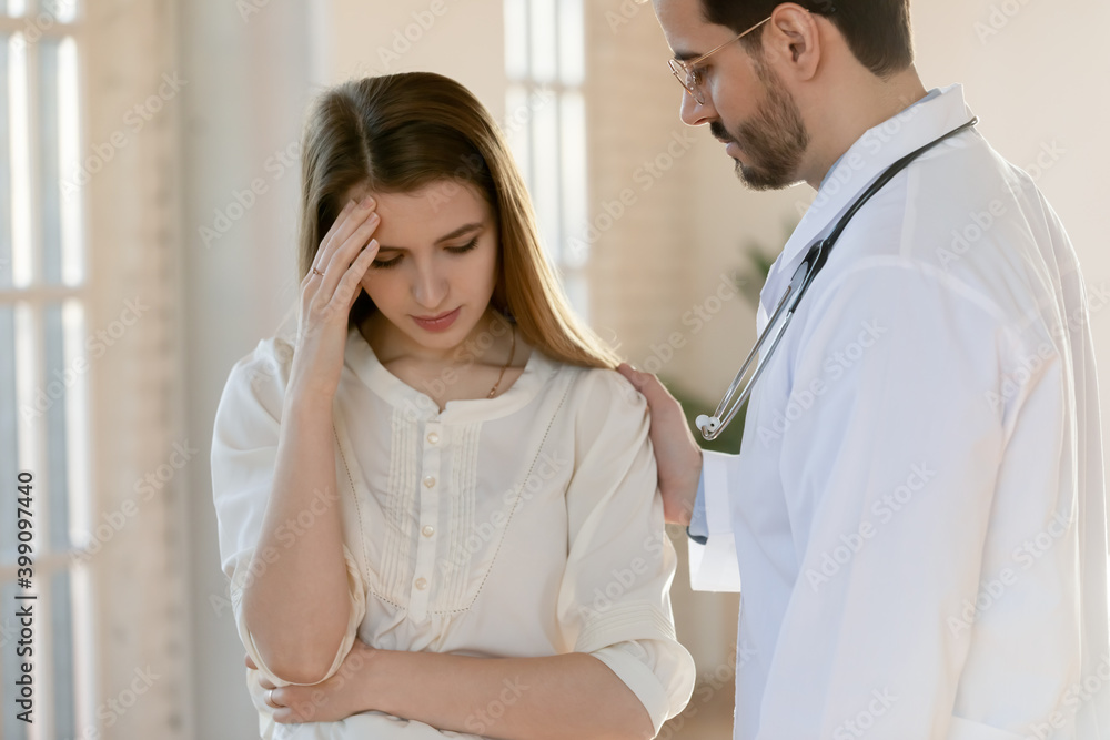 Obraz premium Caring young Caucasian male doctor support comfort unhappy distressed female patient hearing bad news in hospital. Supportive man GP or physician touch show empathy to sad woman client in clinic.