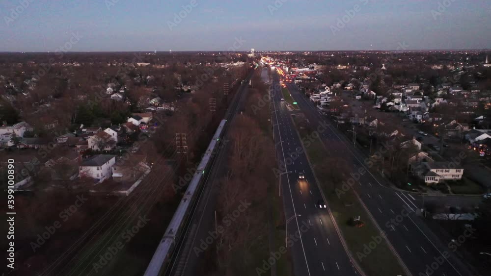A drone view of a treelined path with railroad tracks on one side and a highway on the other. The camera dolly in and tilt down to an oncoming train which passes by during sunset. A drone view of a treelined path with railroad tracks on one side and a highway on the other. The camera dolly in and tilt down to an oncoming train which passes by during sunset.