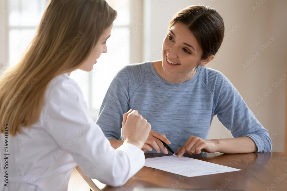 Smiling female patient sign paperwork close deal with doctor at consultation in hospital. Happy young woman client put signature on paper contract make agreement with GP in private clinic. Smiling female patient sign paperwork close deal with doctor at consultation in hospital. Happy young woman client put signature on paper contract make agreement with GP in private clinic.
