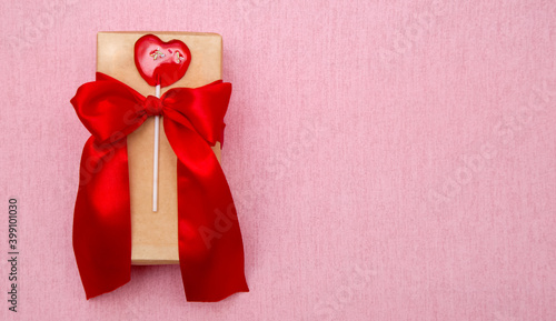 gift box with red bow and lollipop heart on pink background. Copy space. Baner