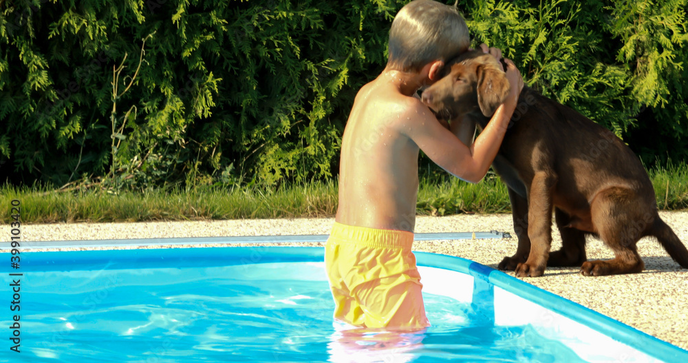 Little boy playing with a dog by the pool. Labrador puppy with baby in the garden.