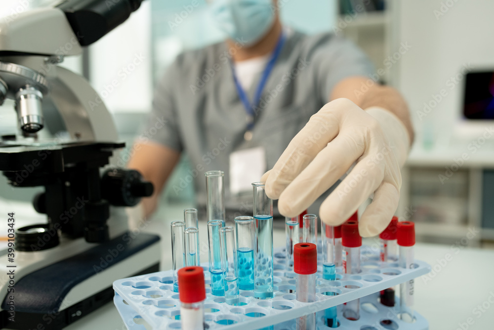 Gloved hand of worker of medical laboratory taking flask with new vaccine Gloved hand of worker of medical laboratory taking flask with new vaccine