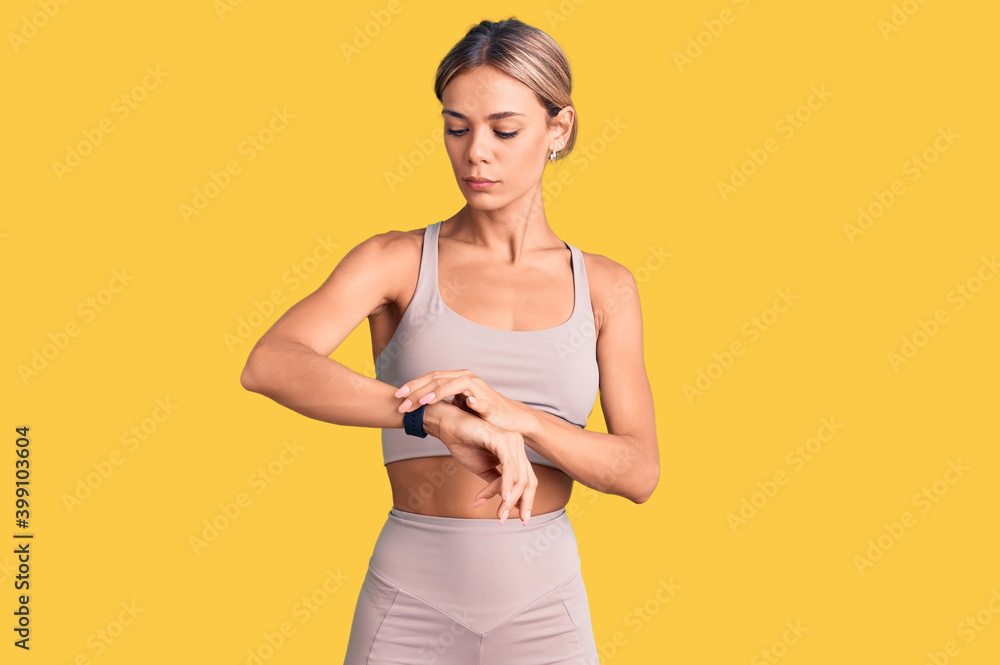 Beautiful caucasian woman wearing sportswear checking the time on wrist watch, relaxed and confident Beautiful caucasian woman wearing sportswear checking the time on wrist watch, relaxed and confident