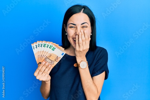 Schilderij op canvas Beautiful young woman holding bunch of 50 euro banknotes laughing and embarrasse