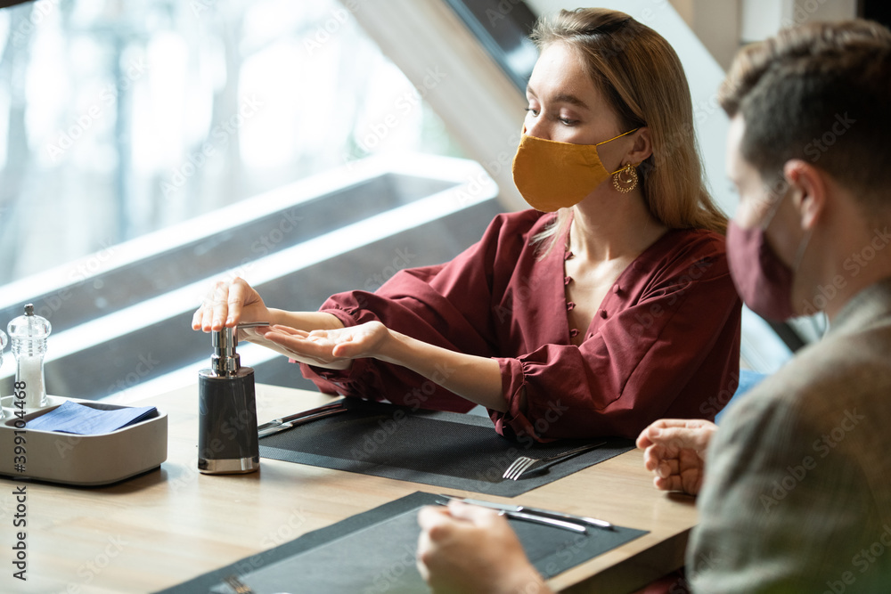 Fototapeta premium Young blond female in smart casualwear and protective mask taking sanitizer