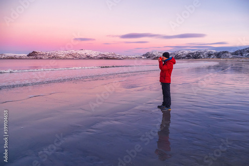 A cup of hot tea in the hand of a man on the Arctic coast against the background of snow-covered Northern hills. Wonderful polar sunset.