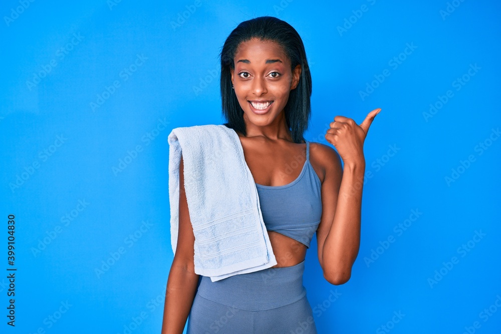Young african american woman wearing sportswear smiling with happy face looking and pointing to the side with thumb up.
