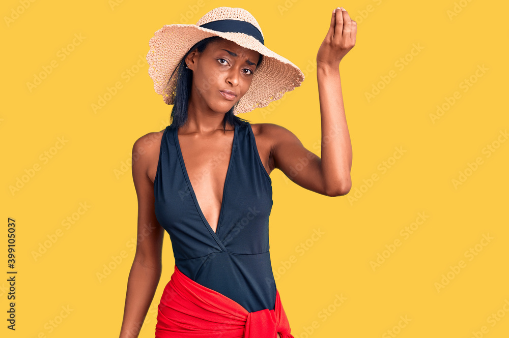 Young african american woman wearing swimsuit and summer hat doing italian gesture with hand and fingers confident expression Young african american woman wearing swimsuit and summer hat doing italian gesture with hand and fingers confident expression
