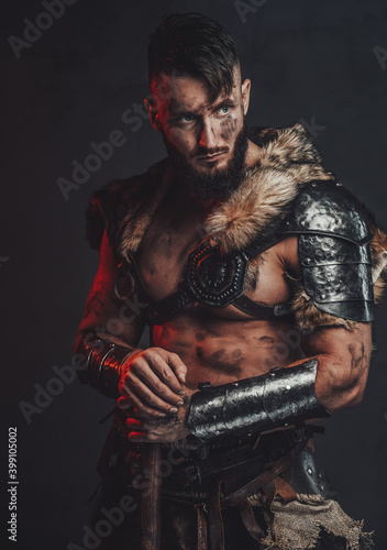 Barbaric and grimy northern vandal in light armour with fur posing in dark background with his two handed axe. © Fxquadro