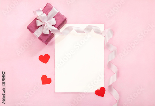 Valentines day greeting card with pink gift box, white bow, long curved ribbon and paper red hearts. Tope view, place for text