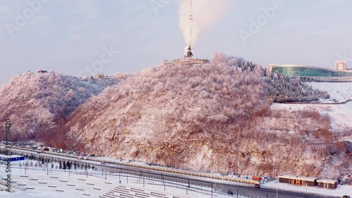 Aerial view of Winter hilly city with roads, trees, monument and buildings. Sunny cold winter day with beautiful cityscape. High quality 4k footage.