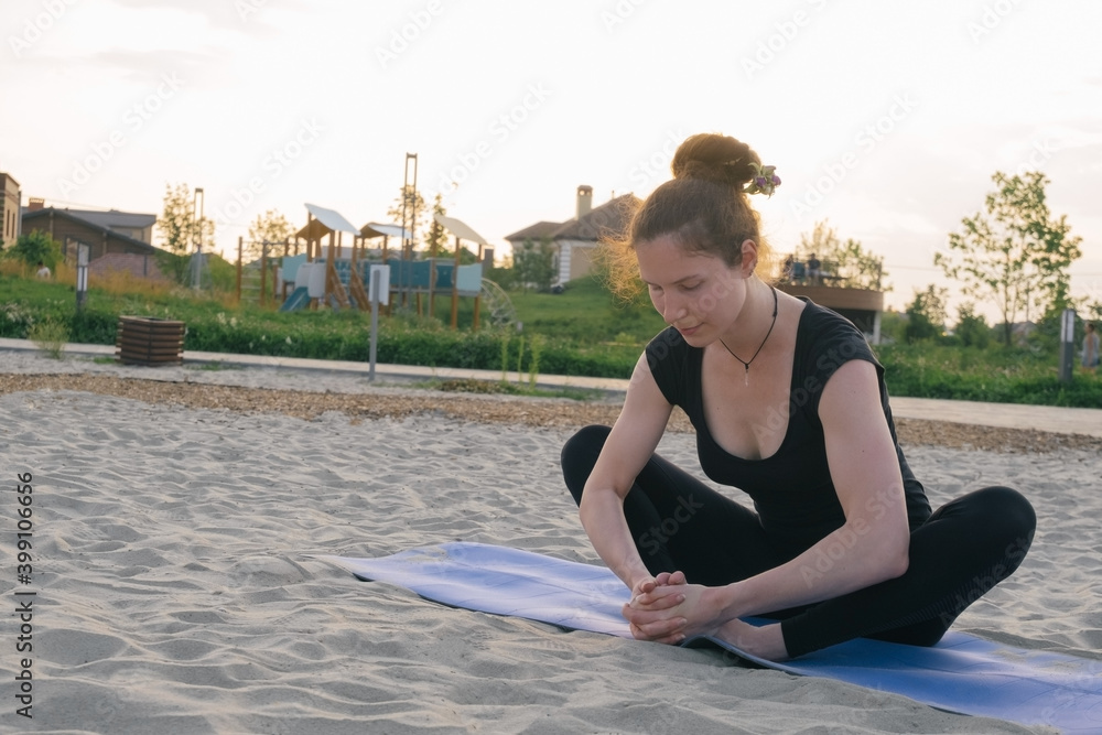 beautiful caucasian woman practising yoga on sand in a city park