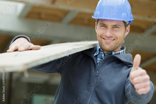 workman carrying wood on his shoulder and showing thumbs-up
