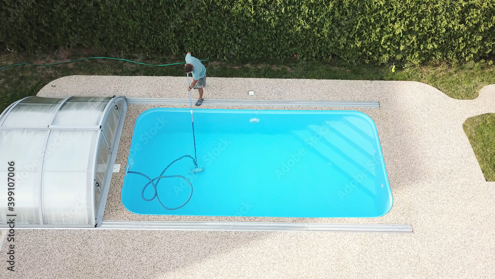 Cleaning the home pool. The man sucks and cleans the swimming pool. Seasonal work from an aerial perspective.
