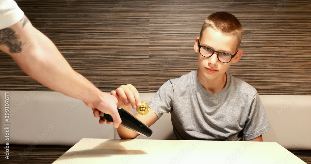 A young boy makes a payment with cryptocurrencies. Use of digital currency for payment. Illustrative bitcoin payment.