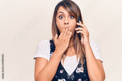 Young beautiful woman having conversation talking on the smartphone covering mouth with hand, shocked and afraid for mistake. surprised expression