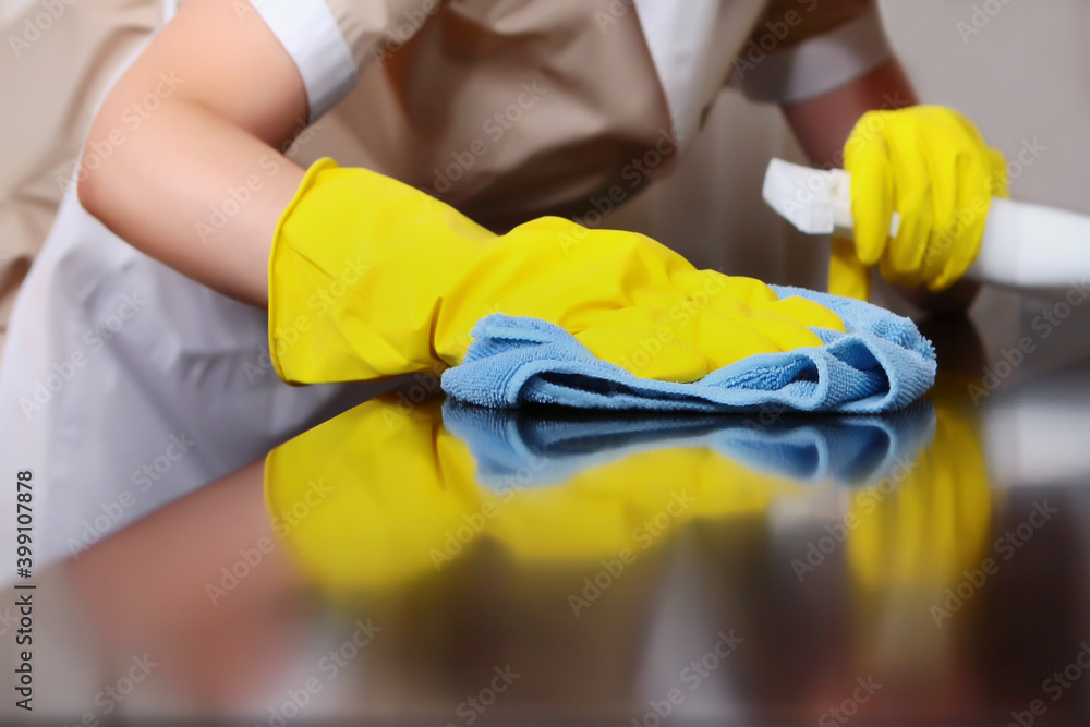 A uniformed maid is dusting the furniture. Cleaning in the hotel room. The person is unrecognizable. Out of focus. The concept of hotel business and cleaning. Hands in protective gloves.