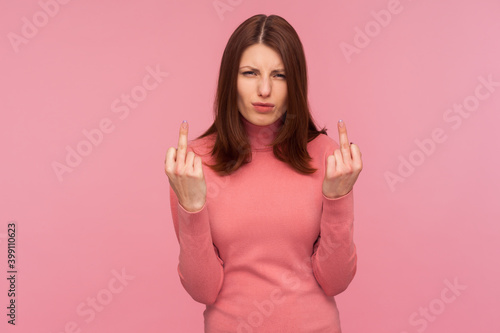 Get off  Angry impolite woman with brown hair in pink sweater showing middle finger looking at camera with aggression and negativity  protest. Indoor studio shot isolated on pink background