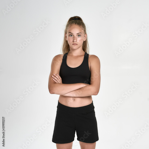 Portrait of cute sportive girl child in black sportswear looking at camera, standing with arms crossed while posing isolated over white background