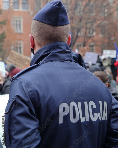 Polish police officer in uniform watching crowd of protesters in the street
