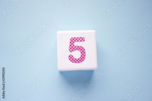 Close-up photo of a white plastic cube with a pink number 5 on a blue background. Object in the center of the photo
