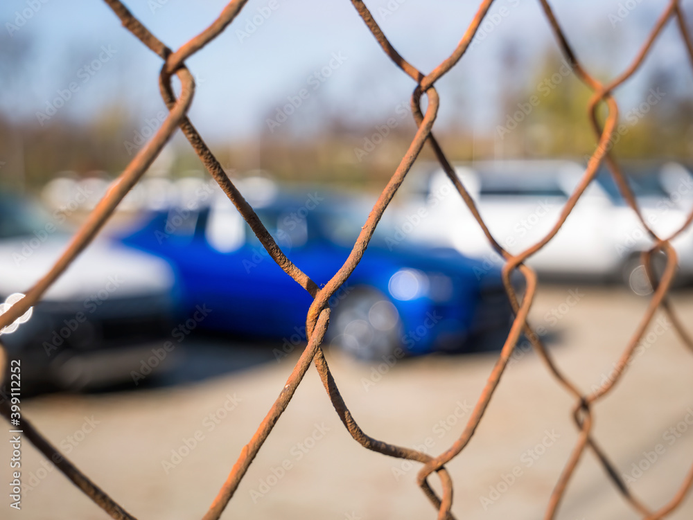Cars parked in a parking lot seen through a rusted wired fence pattern.