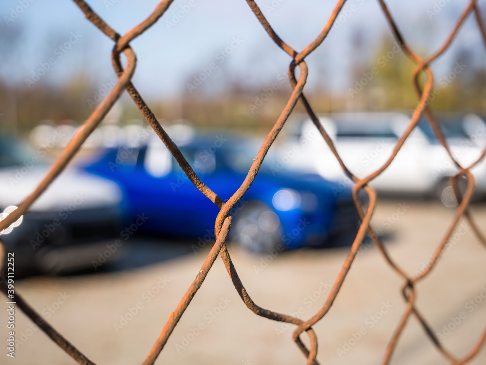 Cars parked in a parking lot seen through a rusted wired fence pattern. Cars parked in a parking lot seen through a rusted wired fence pattern.