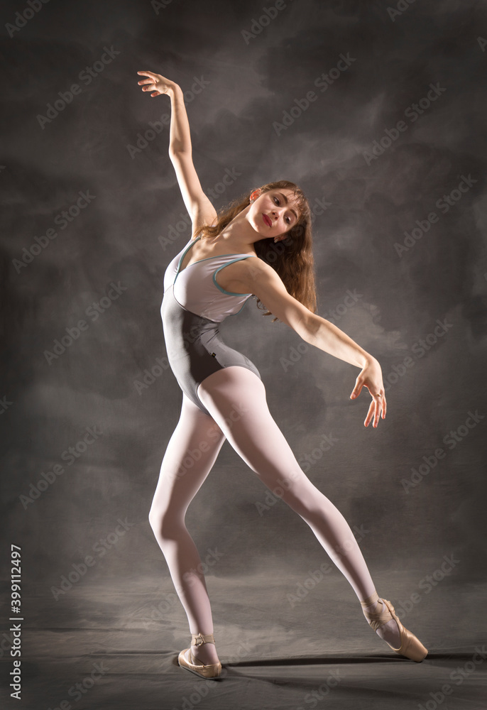 Young adult ballerina in the studio, dancing in gray leotard.