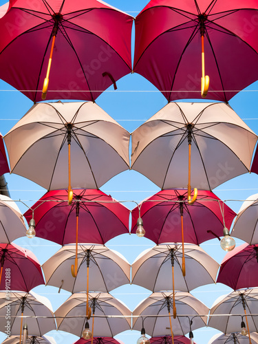 Suspended colored umbrellas and light bulbs against blue sky.