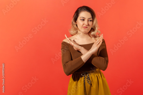 There is no way! Portrait of serious blonde woman in brown blouse crossing hands, gesturing warning or prohibition, meaning stop finish. Indoor studio shot isolated on red background