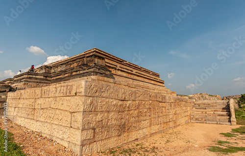 Hampi, Karnataka, India - November 4, 2013: Corner view of Mahanavami Dibba or the Dussehra Platform. Brown stones with sculptures under blue cloudscape. 