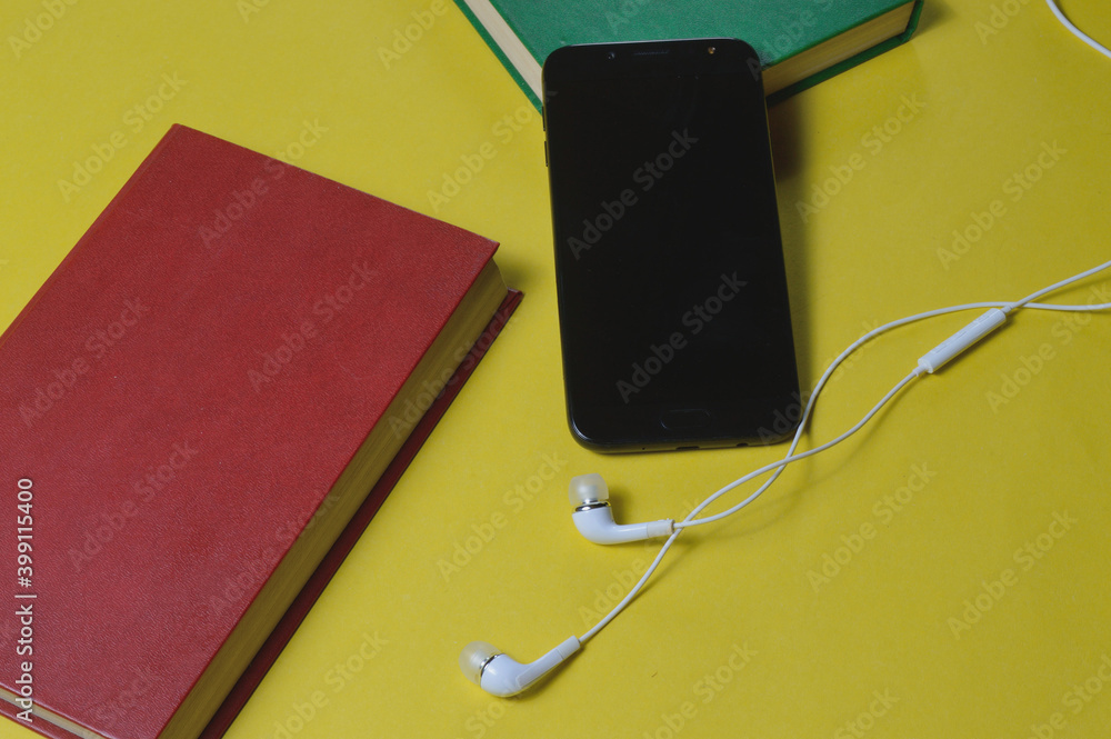 Headphones with books and a smartphone on a yellow background. Headphones with books and a smartphone on a yellow background.
