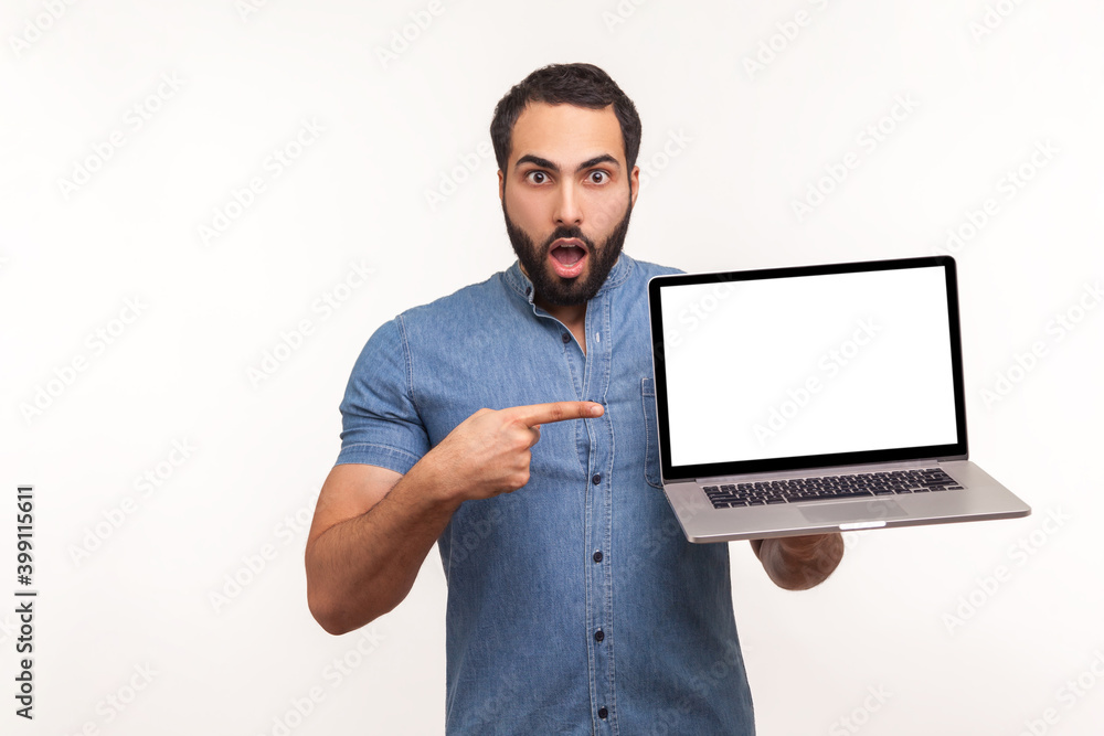 Surprised man pointing finger at empty display of laptop looking at camera with big eyes and opened mouth, shocked with advertisement. Indoor studio shot isolated on white background Surprised man pointing finger at empty display of laptop looking at camera with big eyes and opened mouth, shocked with advertisement. Indoor studio shot isolated on white background