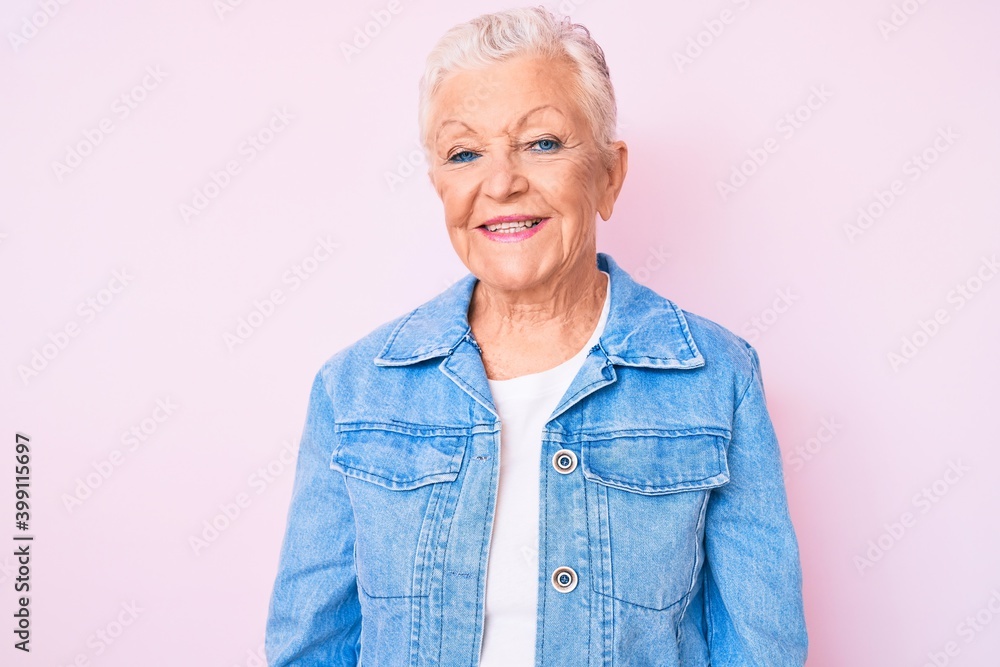 Senior beautiful woman with blue eyes and grey hair wearing casual denim jacket looking positive and happy standing and smiling with a confident smile showing teeth