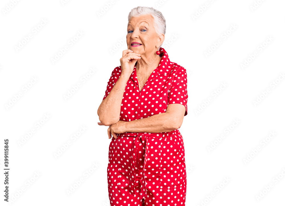 Senior beautiful woman with blue eyes and grey hair wearing a red summer dress looking confident at the camera with smile with crossed arms and hand raised on chin. thinking positive. Senior beautiful woman with blue eyes and grey hair wearing a red summer dress looking confident at the camera with smile with crossed arms and hand raised on chin. thinking positive.
