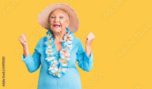 Senior beautiful woman with blue eyes and grey hair wearing summer hat and hawaiian lei screaming proud, celebrating victory and success very excited with raised arms © Krakenimages.com