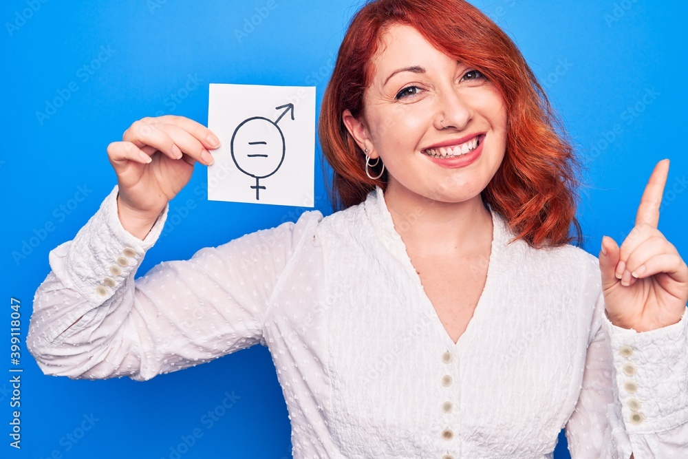 Young redhead woman asking for sex discrimination holding paper with gender equality message smiling happy pointing with hand and finger to the side Young redhead woman asking for sex discrimination holding paper with gender equality message smiling happy pointing with hand and finger to the side