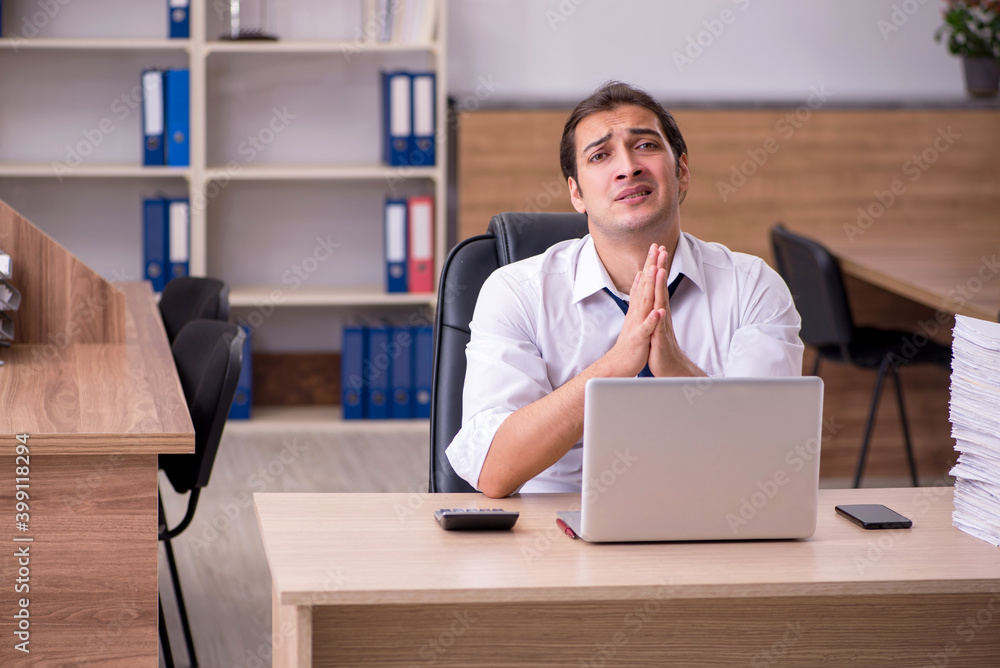 Young male employee unhappy with excessive work in the office Young male employee unhappy with excessive work in the office
