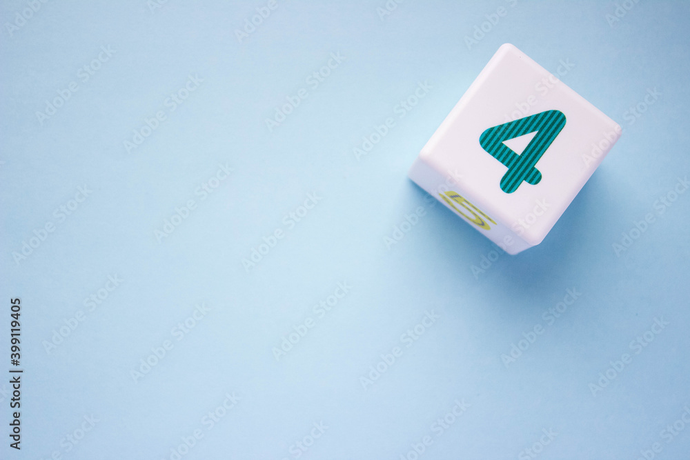 White plastic cube with a green number 4 on a blue background in the upper right corner. With copy space White plastic cube with a green number 4 on a blue background in the upper right corner. With copy space