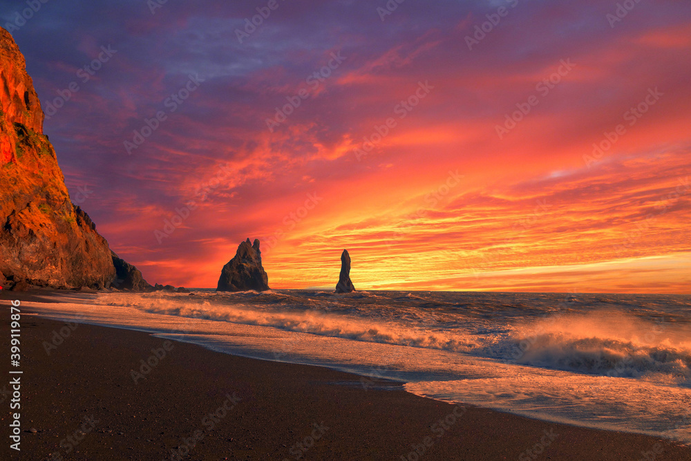 Rock formations jut out of the Atlantic Ocean at the volcanic black sand beach of Reynisfjara near the small town of Vik in Iceland during a beautiful sunset.