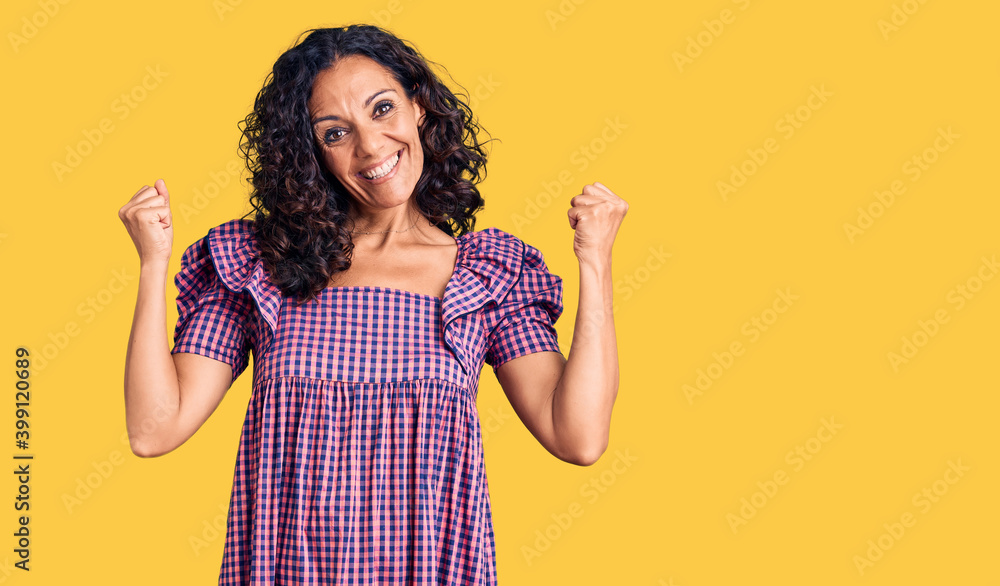 Middle age beautiful woman wearing casual dress screaming proud, celebrating victory and success very excited with raised arms Middle age beautiful woman wearing casual dress screaming proud, celebrating victory and success very excited with raised arms
