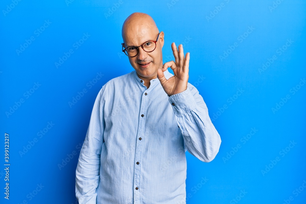 Middle age bald man wearing casual clothes and glasses smiling positive doing ok sign with hand and fingers. successful expression. Middle age bald man wearing casual clothes and glasses smiling positive doing ok sign with hand and fingers. successful expression.