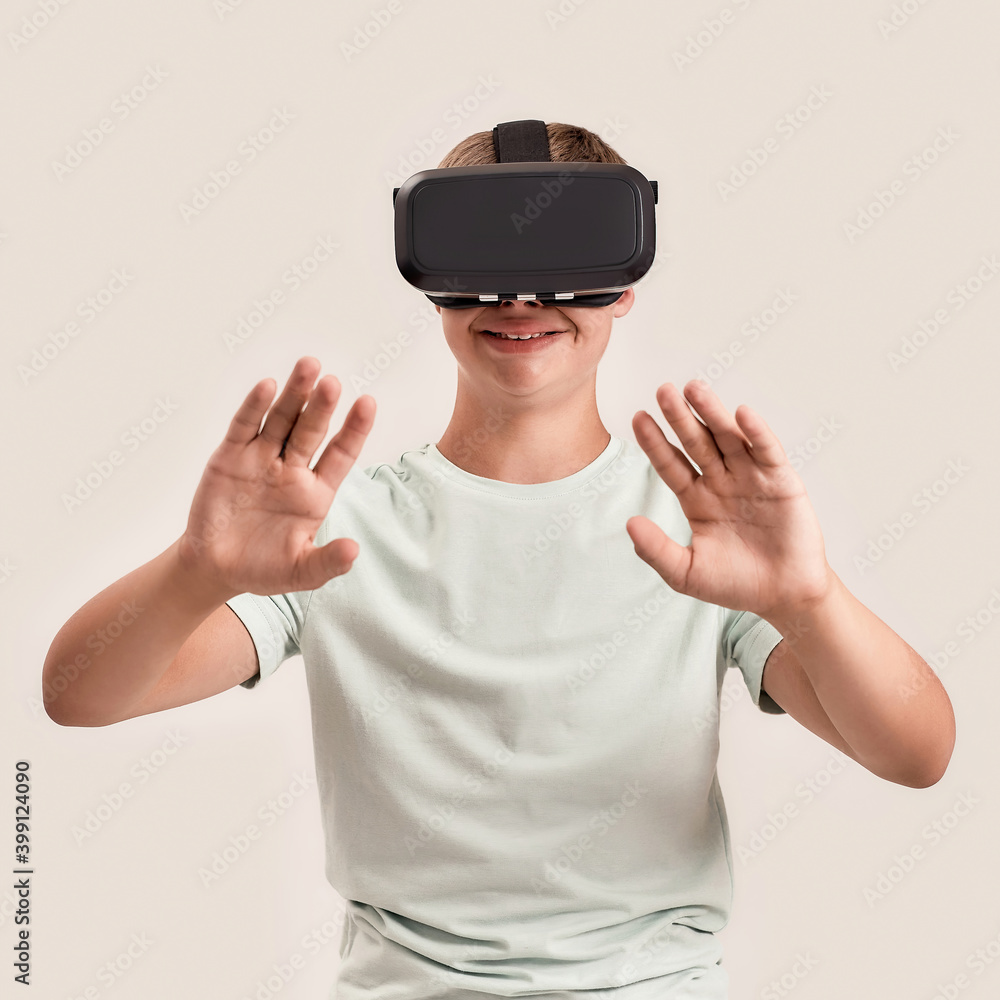 Happy teenaged boy with Down syndrome wearing VR glasses. Special child making gestures while experiencing virtual reality, standing isolated over white background Happy teenaged boy with Down syndrome wearing VR glasses. Special child making gestures while experiencing virtual reality, standing isolated over white background