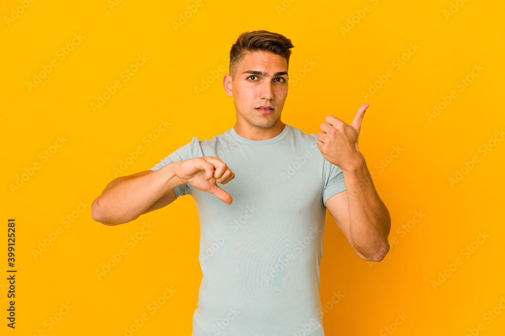 Young handsome caucasian man isolated showing thumbs up and thumbs down, difficult choose concept Young handsome caucasian man isolated showing thumbs up and thumbs down, difficult choose concept